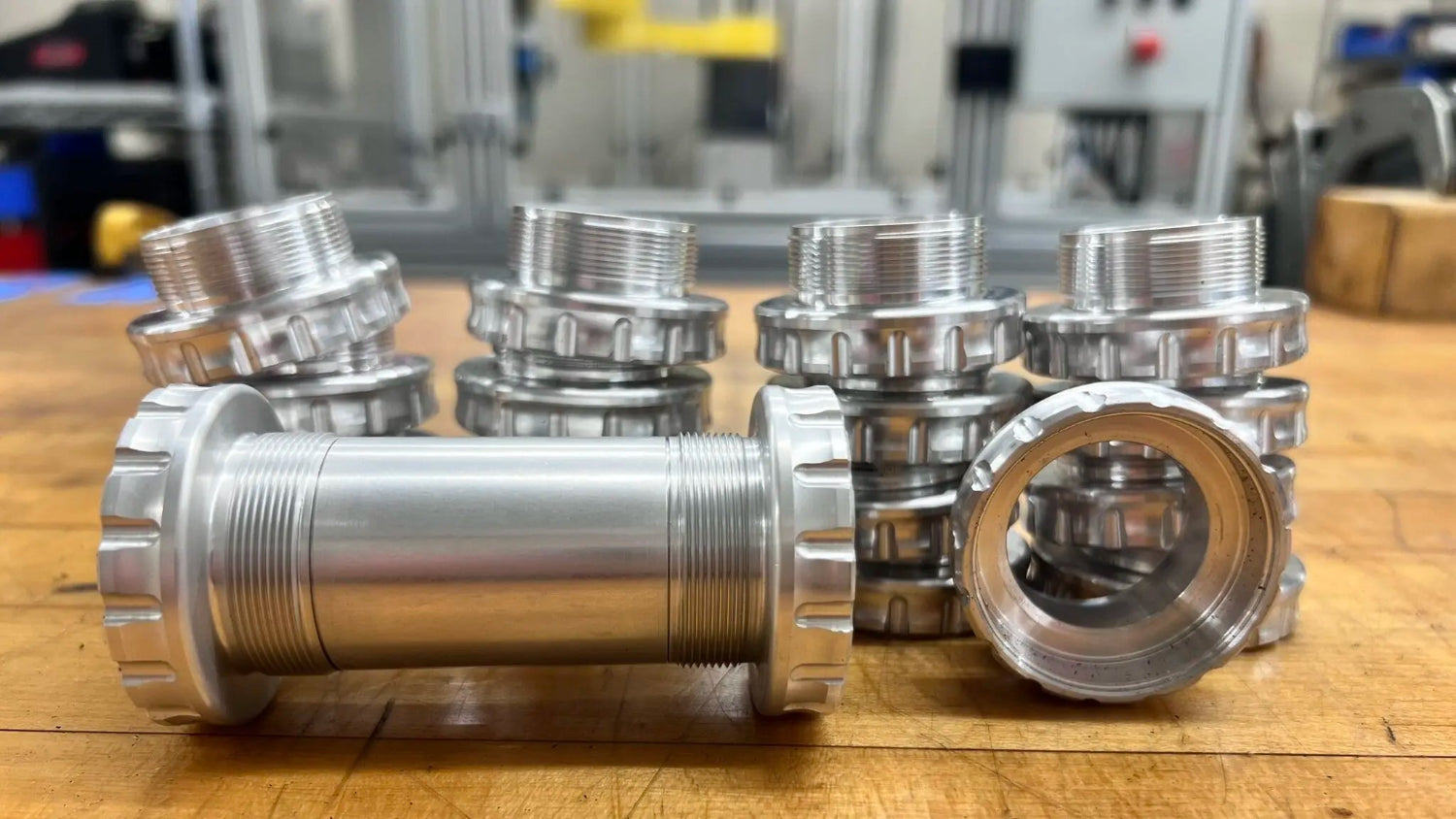 A collection of shiny silver metal bike components with threaded ends arranged on a wooden table in a workshop, conveying precision and craftsmanship.