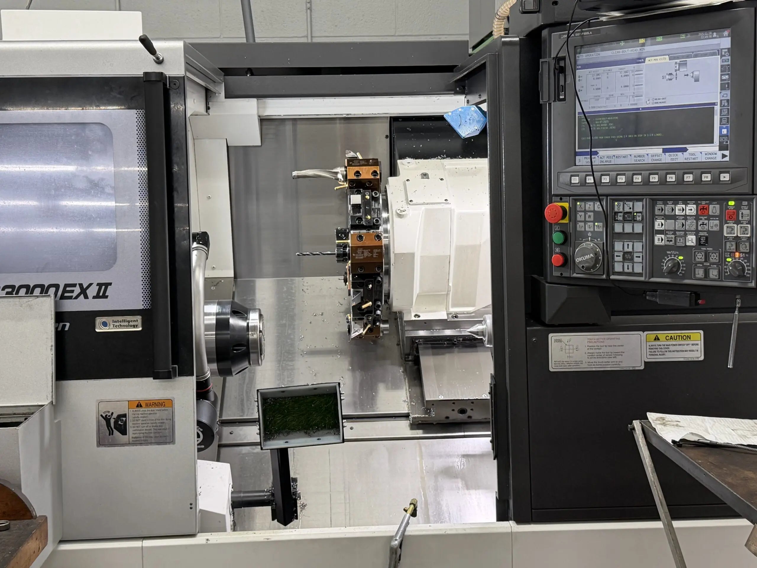 A close-up of a large CNC machine in a workshop, showing its control panel with numerous buttons and screen displaying technical information. The machine's interior features metal components and tools, suggesting industrial precision and high-tech manufacturing.