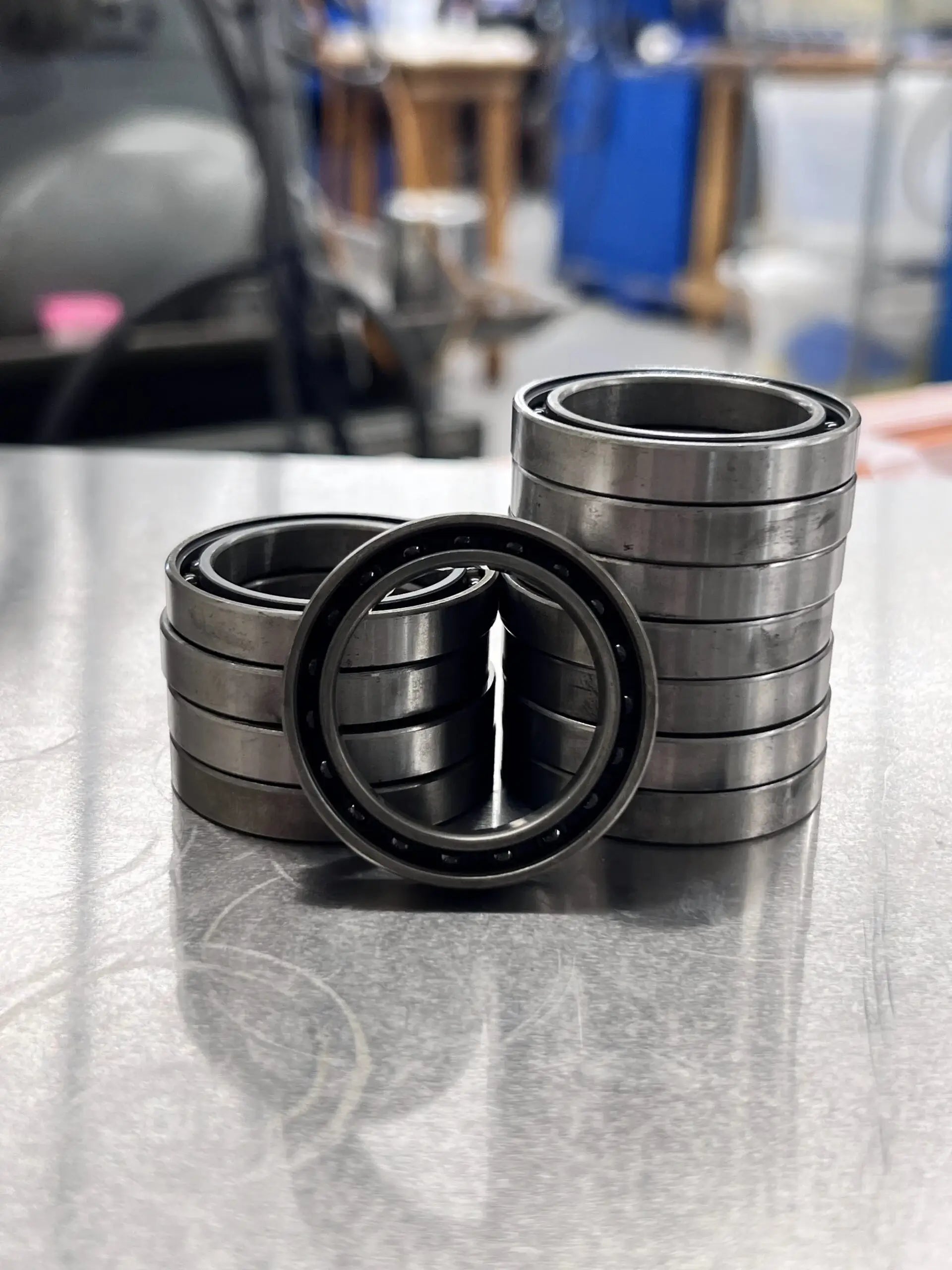 Stacked metal ball bearings on a reflective surface in a workshop. The setting is industrial, with a focus on the smooth, shiny bearings.